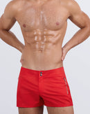 Frontal view of a sexy male model wearing men’s beach shorts in bright red color by the DC2 Miami Menswear brand from Miami.