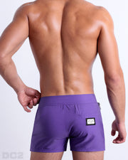 Male model wearing men’s PURPLE MACHINE Beach Shorts swimsuit in a bright purple color, complete the back zippered pocket, made by DC2 a capsule brand by BANG! Clothes in Miami.