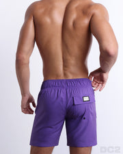 Back view of male model wearing men’s PURPLE MACHINE beach Flex Boardshorts swimming shorts in a solid violet purple color, complete the back pockets, made by DC2 a capsule brand by BANG! Clothes in Miami.