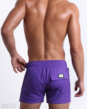 Back view of a male model wearing men’s PURPLE MACHINE Flex Shorts swimsuits in a solid purple color, complete the back pockets, made by DC2 a capsule brand by BANG! Clothes in Miami.
