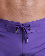 Close-up view of men’s summer Flex shorts by DC2 clothing brand, showing purple color cord with custom-branded golden cord ends, and matching custom eyelet trims in gold.