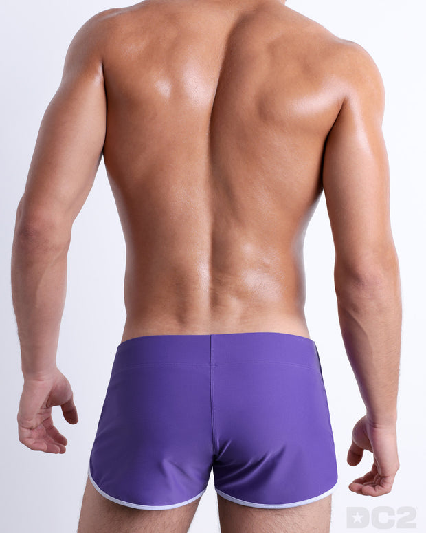 Back view of male model wearing the PURPLE MACHINE beach Swim Shorts for men by BANG! Miami in a solid purple color.