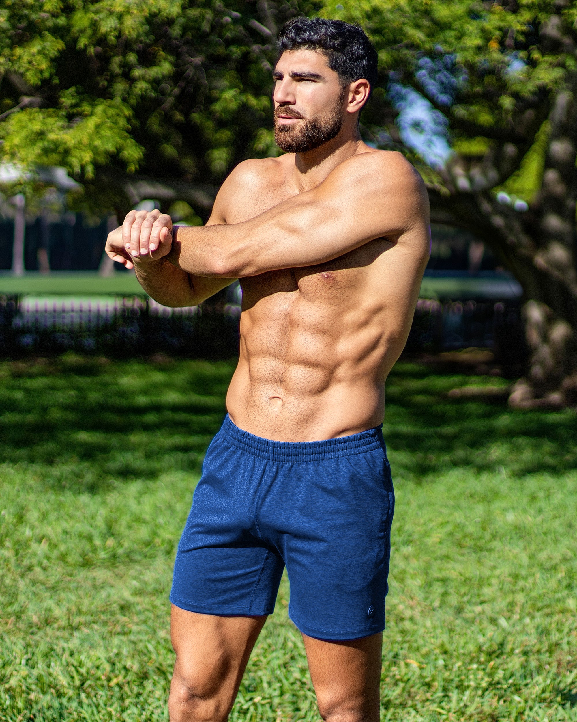 DC2 Miami Physical Blue Jogger Shorts — model wearing navy blue jogger shorts outdoors, stretching in a park setting under sunlight.
