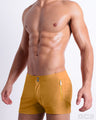 Side view of the RETRO MUSTARD Summer Beach Shorts with dual zippered pockets for men featuring a solid dark yellow color is designed by BANG! Clothes in Miami.