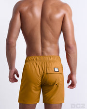 Back view of male model wearing men’s RETRO MUSTARD beach Flex Boardshorts swimming shorts in a solid sunny yellow color, complete the back pockets, made by DC2 a capsule brand by BANG! Clothes in Miami.
