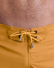 Close-up view of inseam and details of RETRO MUSTARD beach shorts for men, with a mustard yellow color cord and custom branded silver cord-ends, and matching custom eyelet trims in black. 
