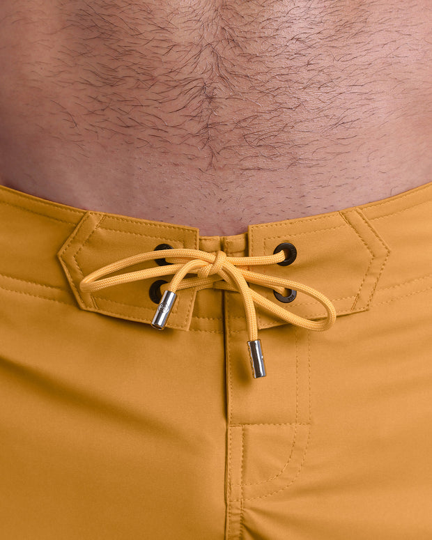 Close-up view of men’s summer Flex shorts by DC2 clothing brand, showing  yellow color cord with custom-branded golden cord ends, and matching custom eyelet trims in gold.