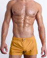 Male model wearing the RETRO MUSTARD Mini Shorts, premium swimwear in a solid sunny yellow color for men. These high-quality swimwear bottoms by DC2, a men’s beachwear brand from Miami.