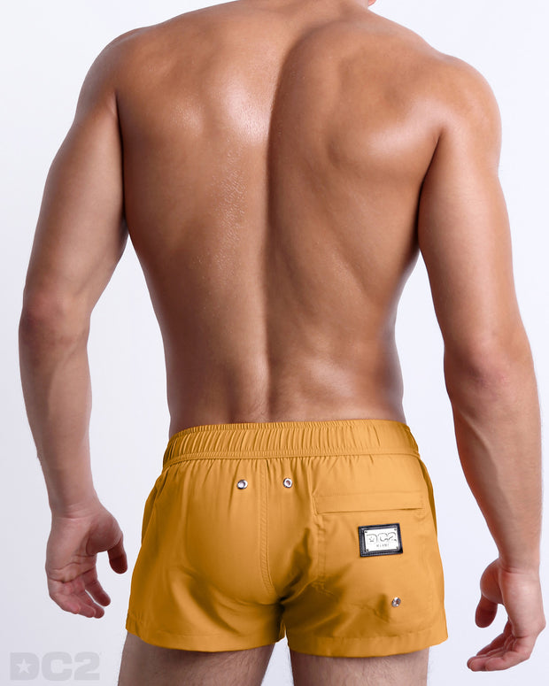 Back view of the RETRO MUSTARD beach Mini Shorts in a solid yellow mustard color, complete with a back zippered pocket, designed by DC2 a capsule brand by BANG! Clothes based in Miami.