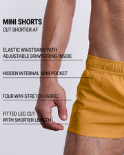 Infographic explaining the many features of the RETRO MUSTARD Mini Shorts. These MINI SHORTS have elastic waistband with adjustable drawstring inside, hidden internal mini-pocket, 4-way stretch fabric, and are quad friendly with fitted leg cut with shorter leg length. 