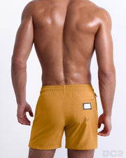 Back view of the RETRO MUSTARD beach Resort Shorts in a solid dark yellow color, complete with a back pocket, designed by DC2 a capsule brand by BANG! Clothes based in Miami.