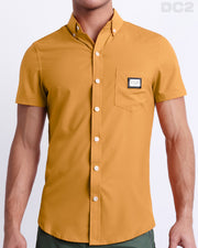 This is a front view of a male model looking sexy in a RETRO MUSTARD stretch shirt for men. The shirt is a solid mustard yellow color on the left pocket. It's a premium quality button-up top made by DC2, a Miami-based men's beachwear brand.
