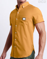 Side view of a masculine model wearing the men’s RETRO MUSTARD Summer button-down shirt in a solid dark yellow color. This high-quality shirt is by DC2, a men’s beachwear brand from Miami.
