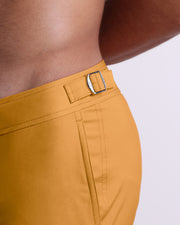Close-up view of the RETRO MUSTARD men’s swimwear, showing custom branded silver metal adjustable side buckles.
