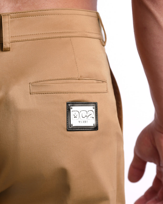 Close up view of cotton fabric chino street shorts back pocket with custom engraved DC2 silver logo plaque.