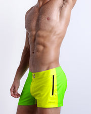 Side view of the SINGLE BILINGUAL (NEON YELLOW/GREEN) men’s summer Beach Shorts, with dual zippered pockets. The shorts are vibrant with fluorescent colors, a bright lime green hue on the right side and a yellow shade on the left made by BANG! Clothes in Miami.