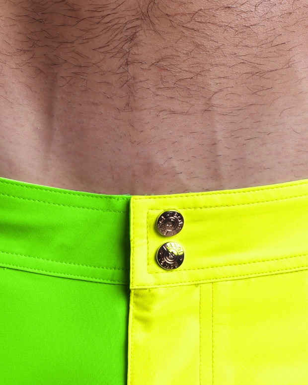 Close-up view of inseam and details of SINGLE BILINGUAL (NEON YELLOW/GREEN) swimsuit for men, showing custom branded golden buttons.