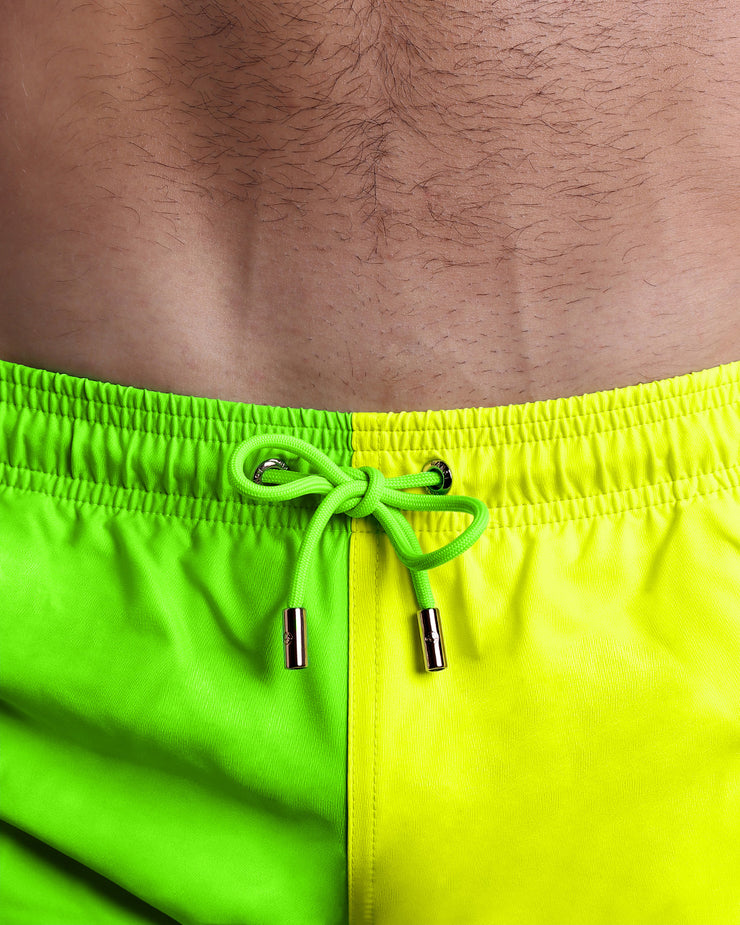 Close-up view of the SINGLE BILINGUAL (NEON YELLOW/GREEN) men’s summer shorts, showing aqua blue cord with custom branded golden cord ends, and matching custom eyelet trims in gold.