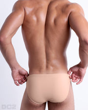 Back view of male model wearing the SKINNY DIP beach mini-briefs for men by BANG! Miami in a solid light cream color.