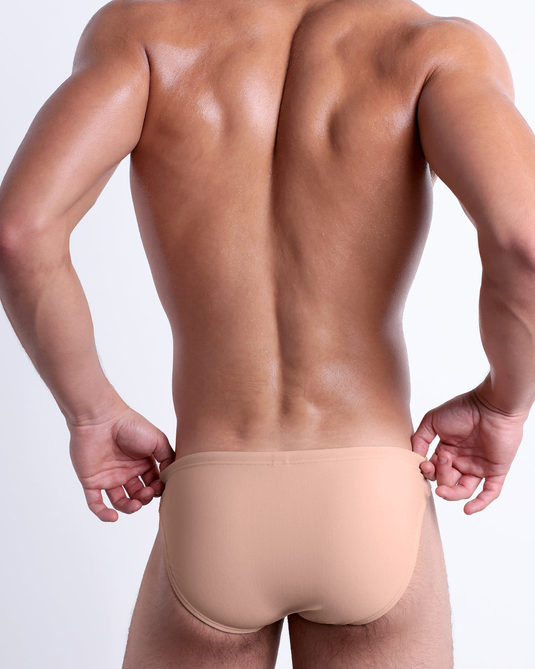 Back view of male model wearing the SKINNY DIP beach mini-briefs for men by DC2 Miami in a solid light cream color.