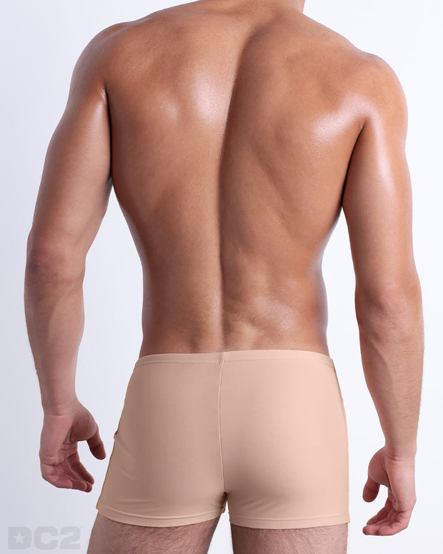 Back view of a male model wearing the SKINNY DIP men’s swim trunks by BANG! Miami in a solid pale tan color.