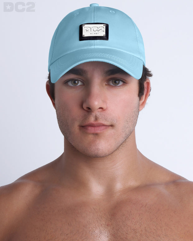 A man wearing the SKY BLUE - Chillax Cap, a stylish light blue color baseball cap made from breathable fabric. The cap features a metallic silver logo plaque on the front and a curved brim for sun protection.