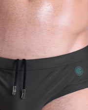 Close-up view of the SLIM GREEN men’s drawstring briefs showing black cord with custom branded metallic silver cord ends, and matching custom eyelet trims in silver.