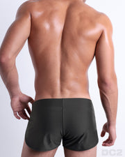 Back view of male model wearing the SLIM GREEN beach Swim Shorts for men by BANG! Miami in a solid dark pine green color.