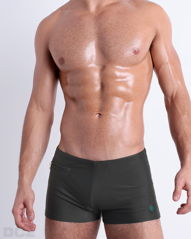 Frontal view of a sexy male model wearing the men’s SLIM GREEN swimsuit with mini pockets in a solid dark green color by DC2, a men&