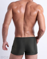 Back view of a male model wearing the SLIM GREEN men’s swim trunks by BANG! Miami in a solid pine green color.