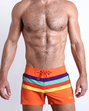 Male model wearing the Stripe'A'Pose REMIX flex shorts in a vibrant orange with colored bands in violet, aqua, red, and yellow by Bang! Miami.