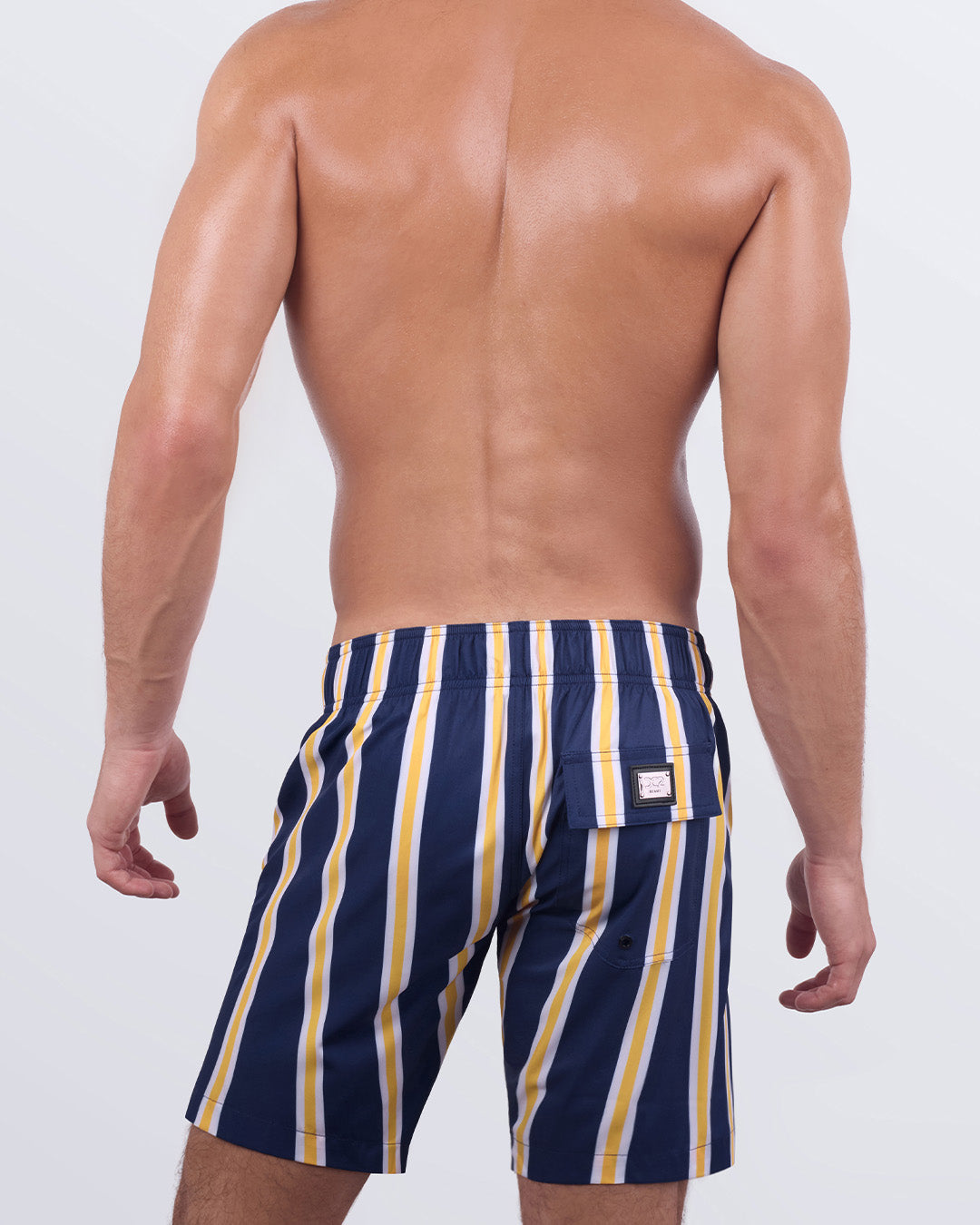 Back view of a male model wearing the SUN CHASING STRIPES Flex Boardshorts by DC2 Miami. These hybrid-style boardshorts feature a comfortable elasticized back waistband, a secure back pocket with a signature DC2 metal logo plaque, and premium quick-dry fabric for all-day wear.