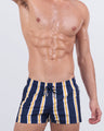 Model wearing SUN CHASING STRIPES Poolside swimming shorts for men, featuring bold navy, white, and yellow vertical stripes.