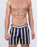 Model wearing SUN CHASING STRIPES tailored swimming shorts for men, featuring bold navy, white, and yellow vertical stripes. These luxury men's swim trunks offer a slim fit with adjustable side buckles, perfect for summer beachwear and resort fashion.