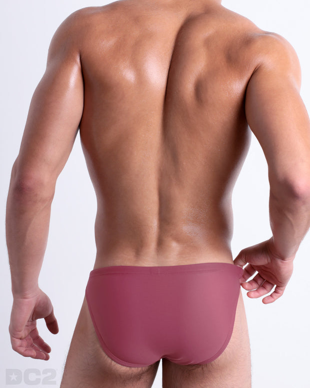 Back view of male model wearing the SUNKISSED RED beach mini-briefs for men by BANG! Miami in a solid rose red color.