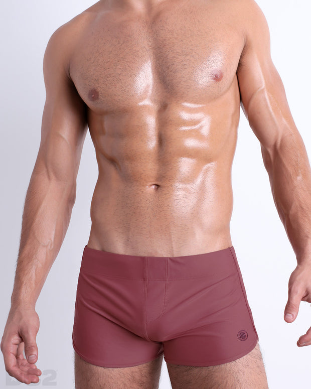 Front view of model wearing the SUN-KISSED RED men’s swimming bottoms in a solid light berry color by DC2, a men&