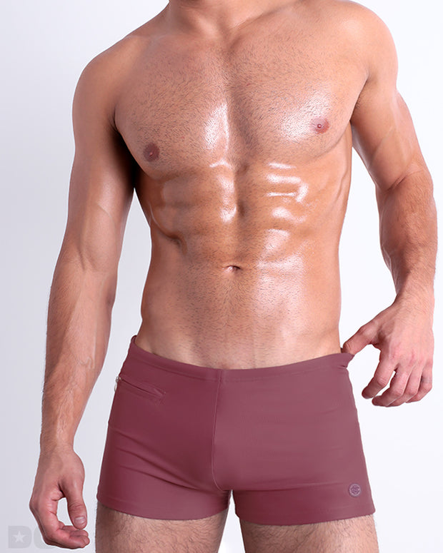 Frontal view of a sexy male model wearing the men’s SUNKISSED RED swimsuit with mini pockets in a solid dark red color by DC2, a men&