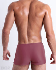Back view of a male model wearing the SUNKISSED RED men’s swim trunks by BANG! Miami in a solid brick red color.