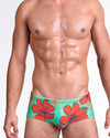 ANG Surf Flowers (Aqua/Red) Swim Sunga — model wearing bold red hibiscus floral print over aqua green gradient base, featuring deep blue outlines and a sleek, body-contouring sunga silhouette.