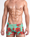 BANG Surf Flowers Aqua Red Swim Trunks — model wearing fitted men’s swim trunks featuring bold red hibiscus florals on a vibrant aqua base.