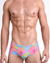 BANG Surf Flowers (Pink/Blue) Swim Sunga — model wearing pink hibiscus floral print on sky blue base, featuring vibrant yellow outlines and a sleek, body-contouring sunga silhouette.