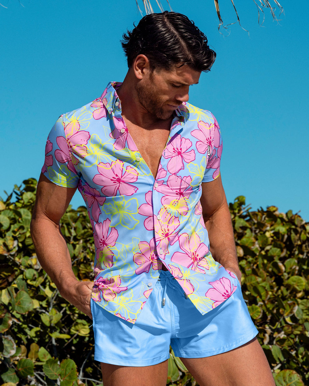Male model wearing the Surf Flowers (Pink/Blue) men’s floral stretch shirt with Magnet Blue men’s poolside shorts.