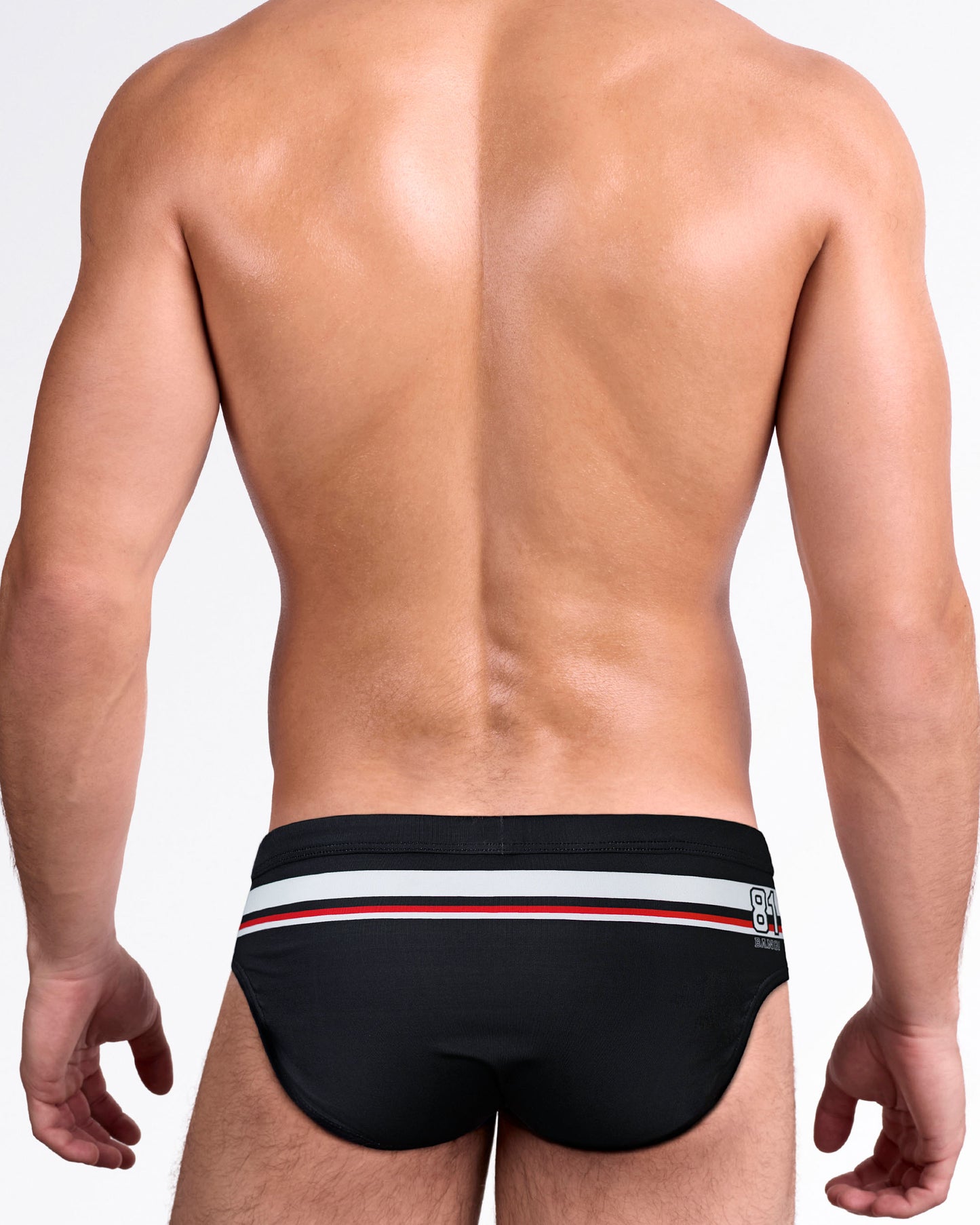 Back view of the BANG Ilya Swim Brief inspired by Heated Revelry, featuring black fabric, racing stripe details, and a streamlined men's swim brief silhouette.