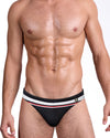 BANG Heated Rivalry Ilya Swim Mini Brief — front view featuring a black body with white and red athletic striping inspired by classic hockey rivalry uniforms.