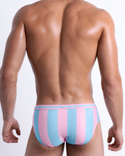 Back view of a male model wearing men’s THE KEN (IBIZA EDITION) Summer swimsuit by BANG! Clothes in Miami, featuring pastel pink and blue colored stripes.
