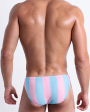 Back view of a male model wearing men’s THE KEN (IBIZA EDITION) Summer swimsuit by BANG! Clothes in Miami, featuring pastel pink and blue colored stripes.