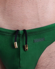 Close-up view of the THE KEN (IBIZA EDITION) men’s summer Swim Mini-Briefs by BANG! clothing brand, showing white cord with custom branded golden cord ends, and matching custom eyelet trims in gold.