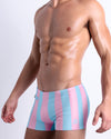 Side view of a male model wearing men’s THE KEN (IBIZA EDITION) sexy Summer beach trunks by BANG! Clothes in Miami, featuring pastel pink and sky blue colored stripes.