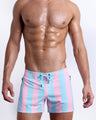 Male model wearing THE KEN (IBIZA EDITION) Flex Shorts, premium swimwear in pink and light blue-colored stripes inspired by the styles seen worn by Ryan Gosling as Ken, in the Barbie movie. Designed by BANG! Clothes, a men’s beachwear brand from Miami.