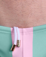 Close-up view of the THE KEN (MALIBU EDITION) men’s summer Swim Mini-Briefs by BANG! clothing brand, showing white cord with custom branded golden cord ends, and matching custom eyelet trims in gold.